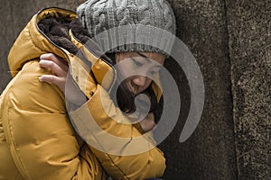 Dramatic lifestyle portrait of young attractive sad and depressed Korean woman in winter hat sitting outdoors on street corner