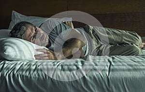 Dramatic lifestyle portrait of young attractive sad and depressed man lying on bed at home bedroom thoughtful and pensive feeling