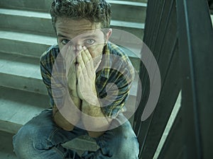 Dramatic lifestyle portrait of young depressed and sad man sitting outdoors on dark street staircase suffering depression problem