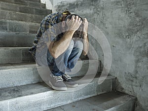 Dramatic lifestyle portrait of young depressed and sad man sitting outdoors on dark street staircase suffering depression problem