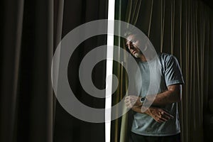 Dramatic light indoors portrait of young sad and depressed attractive man looking through home room window thoughtful and pensive