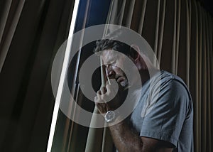 Dramatic light indoors portrait of young sad and depressed attractive man looking through home room window thoughtful and pensive