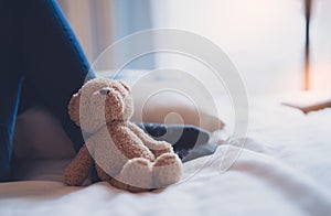 Dramatic Lonely teddy bear lying on kid legs with sunlight shining from window, Sad brown bare lying in bed with in morning,Fluffy