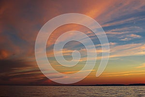 Dramatic clouds on the blue sky in pink yellow red shades in the sunset light on Lake Baikal, beautiful scenic seascape