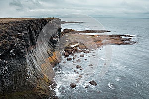 Dramatic mossy cliffs in front of blue ocean in Arnarstapi, Iceland on cloudy day