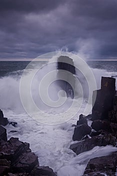 Dramatic nature background - big waves and dark rock in stormy sea, stormy weather. Dramatic scene.