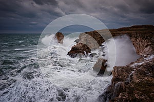 Dramatic nature background - big waves and dark rock in stormy sea, stormy weather. Dramatic scene.