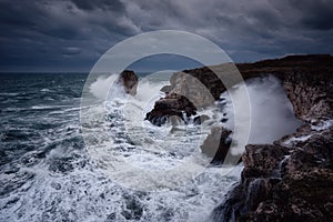 Dramatic nature background - big waves and dark rock in stormy sea, stormy weather. Dramatic scene. Contrasting colors.