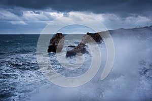 Dramatic nature background - big waves and dark rock in stormy sea, stormy weather. Dramatic scene. Contrasting colors.