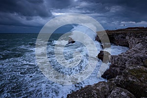 Dramatic nature background - big waves and dark rock in stormy sea, stormy weather. Dramatic scene. Contrasting colors.