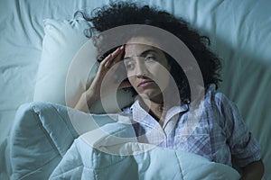 Dramatic night lifestyle potrait of young sad and depressed middle eastern woman with curly hair sleepless in bed awake feeling