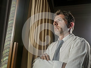 Dramatic night light office portrait of business man working late leaning worried and frustrated on window thoughtful and pensive