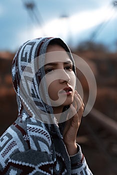 Dramatic outdoor portrait of young teenage hooded girl standing on abandoned old rusty bridge with perspective background.