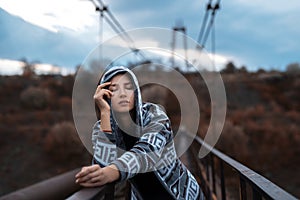 Dramatic outdoor portrait of young, thoughtful hooded girl, standing on old rusty bridge.