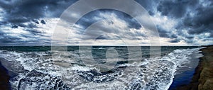 Dramatic overcast sky with nimbostratus clouds and bad weather at panoramic view on the beach with stormy sea waves threatening