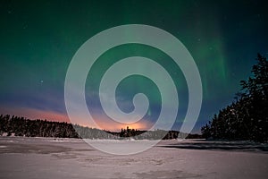 Dramatic polar lights, Aurora borealis with many clouds and stars by moonlight on the sky over a frozen lake and snowy forest in