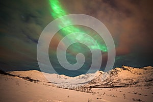 Dramatic polar lights, Aurora borealis with many clouds and stars on the sky over the mountains in the North of Europe - Tromso,