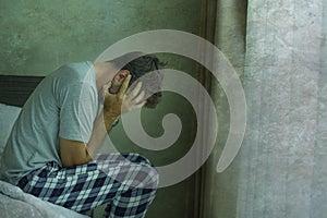 Dramatic portrait of attractive scared and depressed 40s man on bed in pajamas feeling worried suffering anxiety and depression