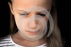 Dramatic portrait of beautiful sad little child girl on the black background, close-up