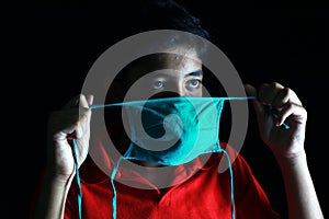 Dramatic portrait of a boy is trying to wear medical face mask looking out deep in thought.