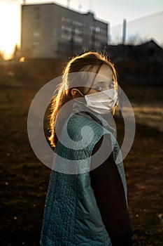 Dramatic portrait of a girl in a mask. A sad girl walks on the street during coratntin. Girl on the background of the setting sun