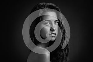 Dramatic portrait of a girl theme: Black and white portrait of a young beautiful girl on a dark background in the studio