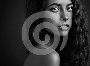 Dramatic portrait of a girl theme: Black and white portrait of a young beautiful girl on a dark background in the studio