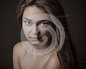 Dramatic portrait of a girl theme: portrait of a beautiful girl with flying hair in the wind against a background in the studio