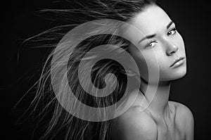 Dramatic portrait of a girl theme: portrait of a beautiful lonely girl with flying hair in the wind isolated on dark background in