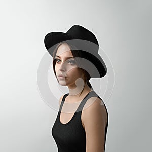 Dramatic portrait of a girl theme: portrait of a beautiful young girl in a black hat and a black shirt on gray background