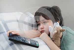 Dramatic portrait Lonely kid sad face holding remote control sitting on couch,child sitting on sofa in living room with looking