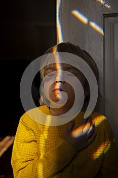 Dramatic portrait of a lonely Ukrainian boy in a yellow sweater in a dark room. sun iridescent glare on the face