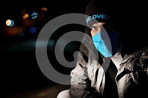 Dramatic portrait of a man in a blue protective mask during quarantine. Night street. Hard light. Coronavirus. Quarantine. Caption