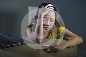 Dramatic portrait scared and stressed Asian Korean teen girl or young woman with laptop computer and mobile phone suffering cyber