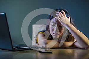 Dramatic portrait scared and stressed Asian Korean teen girl or young woman with laptop computer and mobile phone suffering cyber