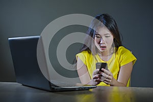 Dramatic portrait scared and stressed Asian Korean teen girl or young woman with laptop computer and mobile phone suffering cyber