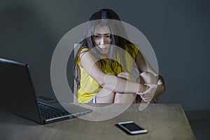 Dramatic portrait scared and stressed Asian Korean teen girl or young woman with laptop computer and mobile phone suffering cyber