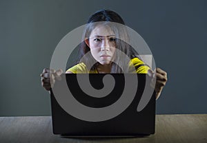 Dramatic portrait of scared and stressed Asian Korean teenager girl or young woman with laptop computer suffering cyber bullying s