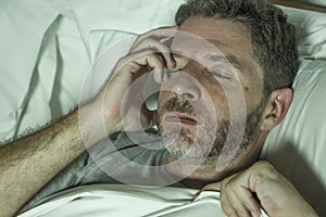 Dramatic portrait of stressed and frustrated man in bed awake at night suffering insomnia sleeping disorder tired and desperate