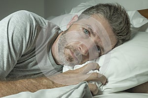 Dramatic portrait of stressed and frustrated man in bed awake at night suffering insomnia sleeping disorder tired and desperate