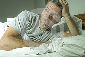 Dramatic portrait of stressed and frustrated man in bed awake at night suffering insomnia sleeping disorder tired and desperate