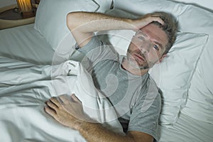 Dramatic portrait of stressed and frustrated man in bed awake at night suffering insomnia sleeping disorder tired and desperate