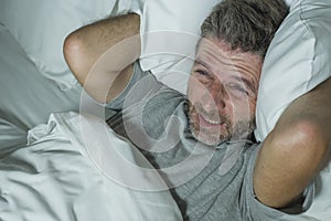 Dramatic portrait of stressed and frustrated man in bed awake at night suffering insomnia sleeping disorder tired and desperate