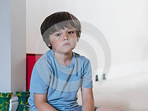 Dramatic portrait tired kid siting alone and lookig out deep in throught, Bored child siting on floor with unhappy face, Lonely