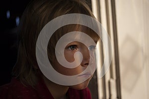 Dramatic portrait of an upset lonely boy of 6 years old in a dark room, accentuated by a streak of ligh