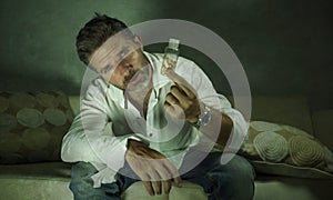 Dramatic portrait of young attractive depressed and wasted pills addict man holding antidepressant tablets bottle sitting on couch