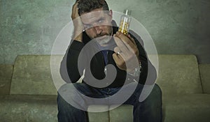 Dramatic portrait of young attractive depressed and wasted pills addict man holding antidepressant tablets bottle sitting on couch