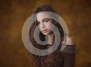 Dramatic portrait of a young beautiful brunette girl with long curly hair in the studio.