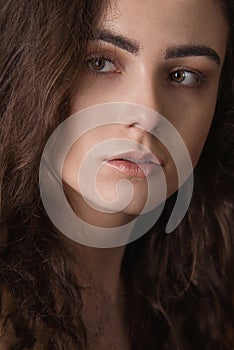 Dramatic portrait of a young beautiful brunette girl with long curly hair in the studio.