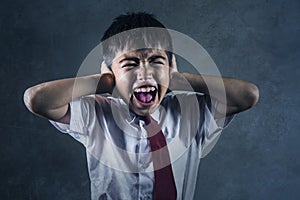 Dramatic portrait of young desperate and abused schoolboy in uniform crying alone victim of bullying and abuse at school